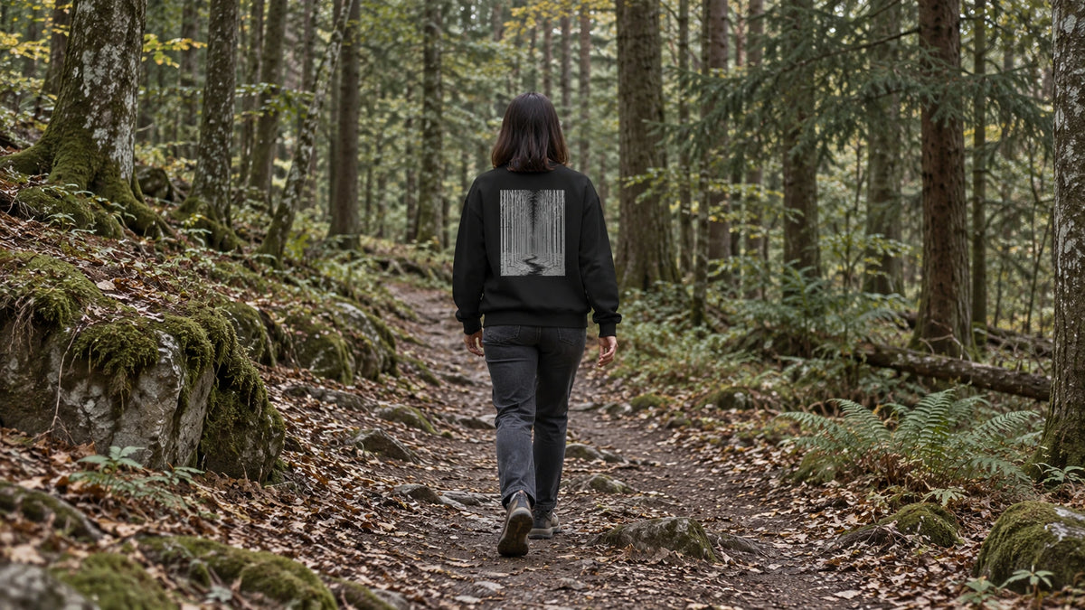Eine Frau im schwarzen Eintritt-in-den-Wald-Sweatshirt geht auf einem natürlichen Waldweg.